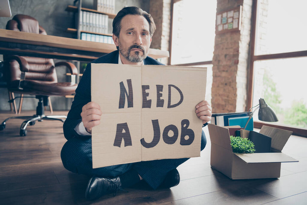 Portrait of his he depressed jobless guy banker sitting on wooden floor holding placard need a job words begging new work place at modern loft industrial brick style interior workplace workstation - Foto, Bild