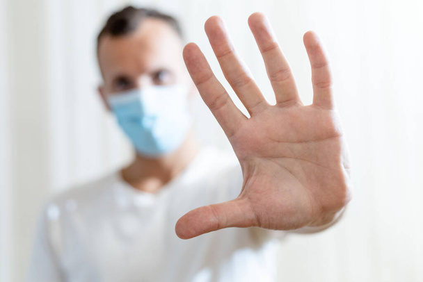 hombre borroso en máscara médica muestra gesto de parada de la palma abierta sobre fondo claro - Foto, Imagen