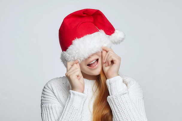 attractive red-haired teenage girl in a Santa hat. The concept of Christmas and the New year. photo session in the Studio on a white background - Foto, imagen