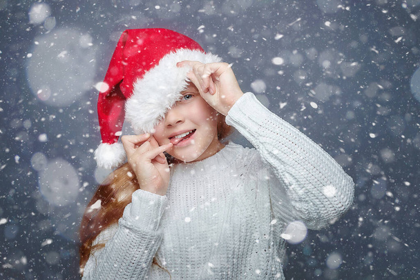 happy red-haired teenage girl in a Santa hat. photo session in the Studio with simulated snowfall - Фото, зображення