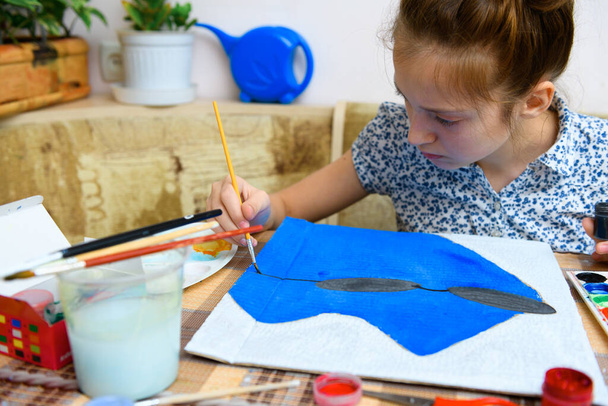 ένα κορίτσι που σχεδιάζει μπλε χαρτόνι γκουάς, καλλιτεχνική δημιουργία στο σπίτι, κάνει δημιουργικό έργο τέχνης - Φωτογραφία, εικόνα