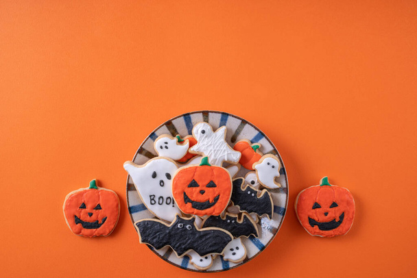 Top view of Halloween festive decorated icing gingerbread sugar cookies on orange background with copy space and flat lay layout. - 写真・画像