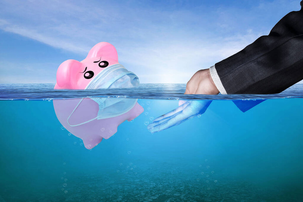 Financial Aid and rescue from debt problems for investments above water as a drowning pink piggy bank sinking in blue water. Concept of financial crisis after coronavirus covid-19 pandemic.  - Photo, Image