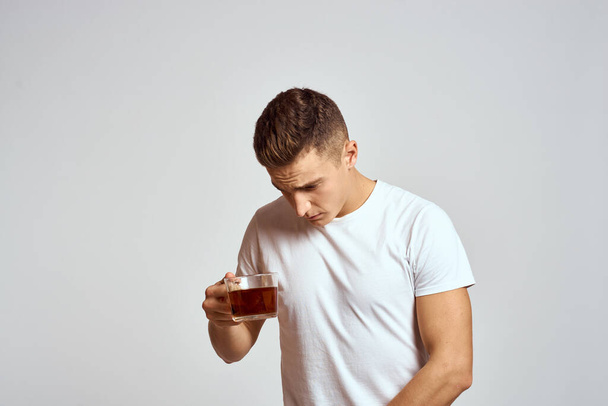 Elinde bir fincan çay ve beyaz tişörtle başını eğen bir adam. - Fotoğraf, Görsel
