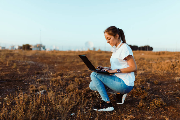 Mujer joven con su portátil se comunica con las antenas en el campo - Foto, Imagen