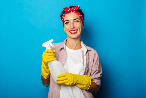 Jeune femme souriante tenant pulvérisation dans des gants sur fond bleu - Photo, image