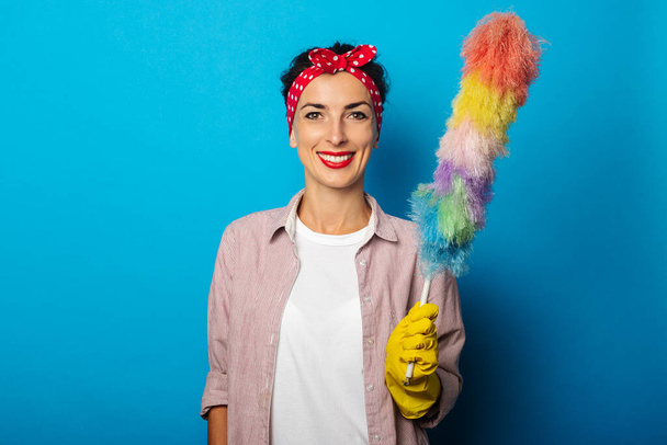 Smiling young woman in gloves holding dust brush on blue background - Photo, Image