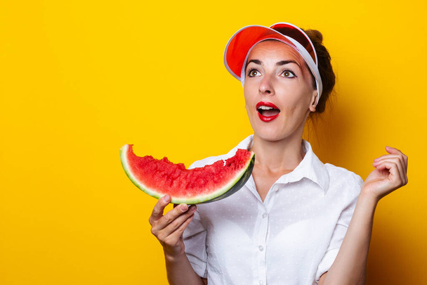 Young woman in red visor holding a slice of watermelon on yellow background - Photo, Image
