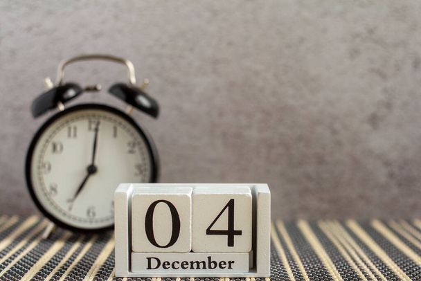 4 dicembre su un calendario di legno accanto a una sveglia su un tavolo buio. Un giorno d'inverno. Spazio per il testo. - Foto, immagini