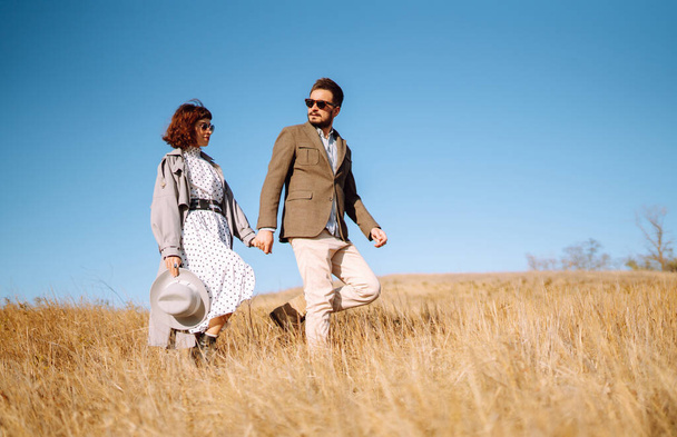 Stylish  young couple enjoying autumn weather in autumn field. Lovely couple walking and hugging in the field together. The concept of youth, love and lifestyle. - Zdjęcie, obraz