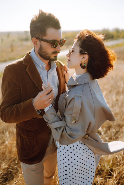 Stylish  young couple enjoying autumn weather in autumn field. Lovely couple walking and hugging in the field together. The concept of youth, love and lifestyle. - Foto, imagen