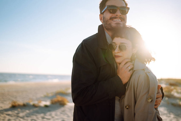 Young loving couple walking and hugging by the sea. Enjoying time together. Fashion, lifestyle and autumn mood. - Foto, imagen