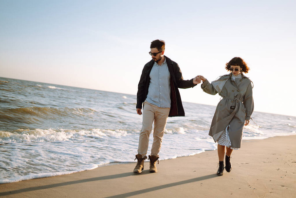 Young loving couple walking and hugging by the sea. Enjoying time together. Fashion, lifestyle and autumn mood. - Fotó, kép
