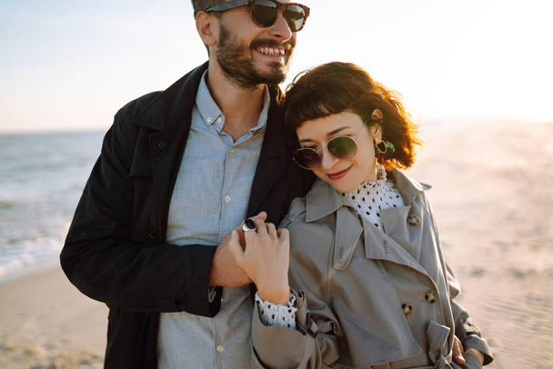 Young loving couple walking and hugging by the sea. Enjoying time together. Fashion, lifestyle and autumn mood. - Valokuva, kuva