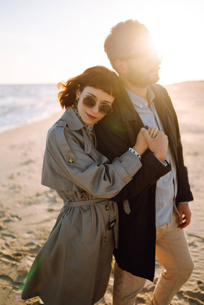 Young loving couple walking and hugging by the sea. Enjoying time together. Fashion, lifestyle and autumn mood. - Photo, Image