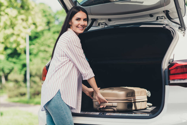Photo of positive girl have summer time vacation put suitcase car trunk ready travel airport air flight camp in city center outdoors - Φωτογραφία, εικόνα