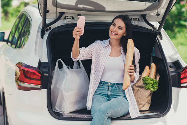 Portrait of her she nice attractive cheerful cheery lady blogger sitting in trunk carrying fresh bread ingredients bio farm products baguette supply taking making selfie outdoor outside - Foto, imagen