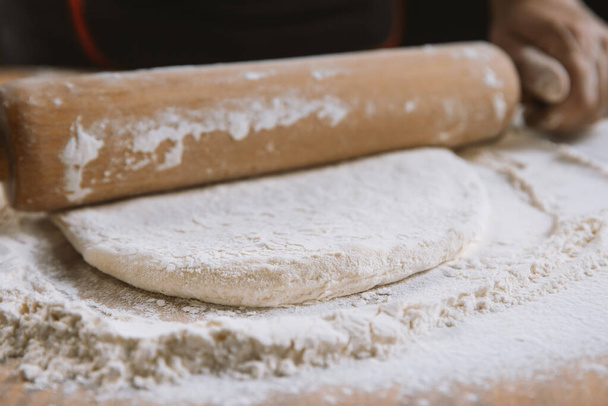 Baker kneading dough for pizza preparation. Chef cook making dough for baking pie on wooden table. Process preparation homemade pastry. Cooking pasta, bread,spaghetti,khachapuri, food concept - Photo, Image