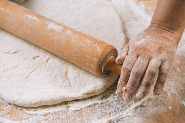 Chef is rolling the dough with the rolling pin on the on the table. Hands close-up.Cooking pasta, bread,spaghetti,khachapuri, food concept - Foto, afbeelding