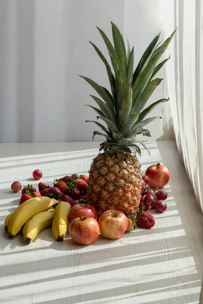 köstliche frische Früchte auf weißem Hintergrund mit Sonne, Ananas, Bananen, Apfel, Erdbeere, Trauben und Bananen, gesunde Ernährung - Foto, Bild