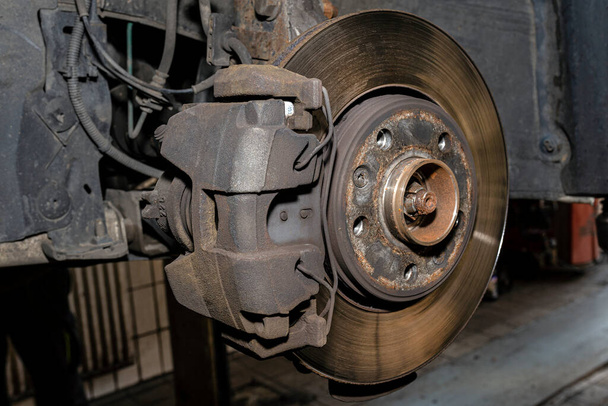 Ancien disque de frein avant avec étrier et plaquettes de frein dans la voiture, sur un ascenseur de voiture dans un atelier. - Photo, image