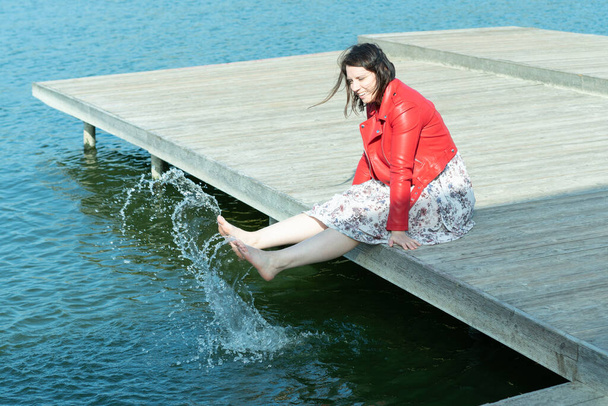 eine Frau, die auf einer Brücke sitzt und ihre Beine ins Wasser baumelt - Foto, Bild