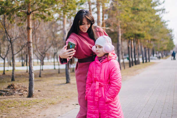 Mamá y su hija se toman una selfie en el parque. El niño camina con su madre en invierno. - Foto, Imagen