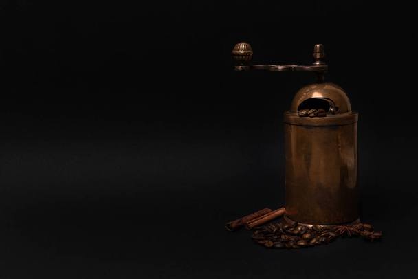 Moinho de café manual antigo, grãos espalhados, paus de canela, sementes de anis em cores escuras. Espaço de cópia - Foto, Imagem