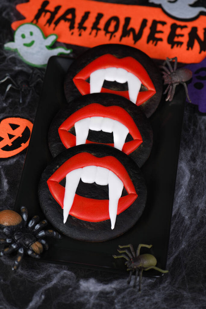 Vampirzähne, die aus scharlachroten Lippen herausragen, glasierte Honig-Lebkuchen. Idee zu Halloween-Essen - Foto, Bild
