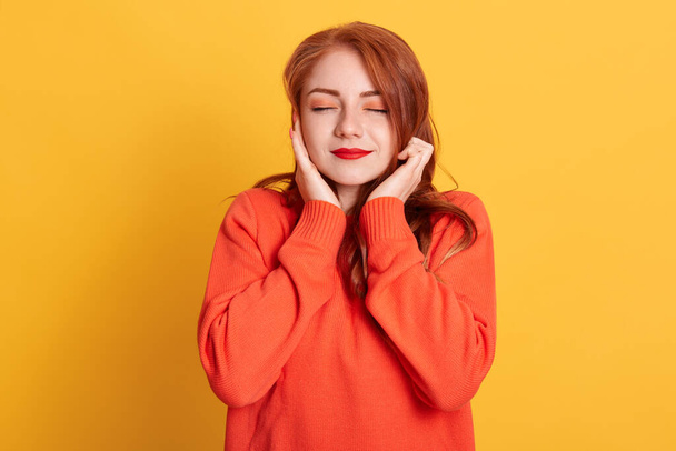 Red haired woman plugging ears with fingers and closing her eyes, not wanting to listen hard loud music, ignoring noise or avoiding loud sounds, wearing casual sweater. - Foto, Imagen