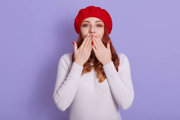 Attractive gorgeous woman blows sweet kiss at camera, flirts with somebody, says goodbye. Adorable female sends kiss to you, winsome red haired female in beret against lilac wall. - Fotoğraf, Görsel