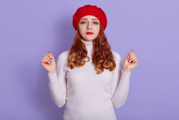 Girl with french style over lilac wall feeling upset, looking at camera with sad expression, wearing red beret and white shirt, has beautiful curly hair, has bed news. - Photo, Image