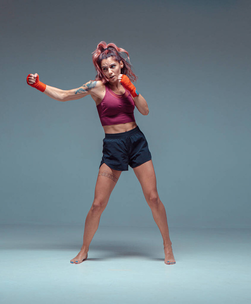 Female fighter trains in boxing bandages in studio on gray background. - Photo, image