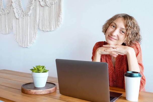 Aantrekkelijke jonge vrouw typt berichten op een laptop bij de grote ramen van een koffieshop. Hipster meisje werken op een laptop in een cafe. - Foto, afbeelding