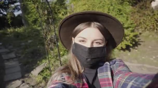 La mujer usa máscara protectora al aire libre durante la pandemia del covid-19 del coronavirus. Chica disfruta de caminar en otoño parque filmándose. - Metraje, vídeo