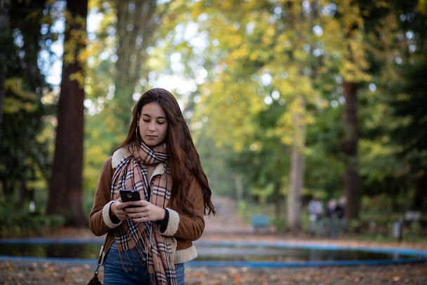 молодая женщина в осеннем пейзаже на смартфоне - копировальное пространство - селективный фокус - Фото, изображение
