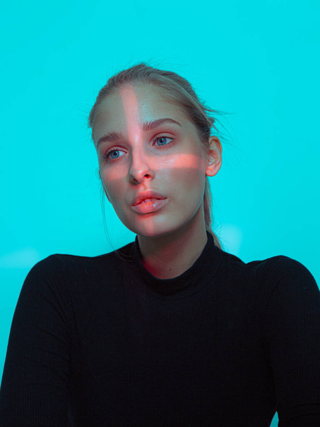Cool girl with cross shaped light on her face on blue studio background - 写真・画像
