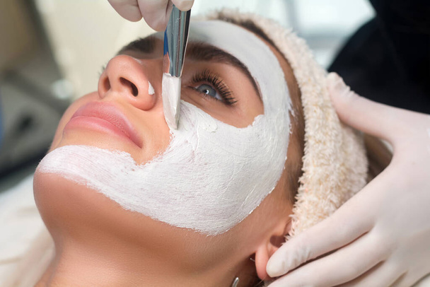 Een masker op het gezicht aanbrengen in een schoonheidssalon. Cosmetoloog en procedure voor verjonging en hydraterende. - Foto, afbeelding