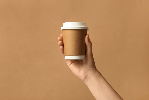 Woman holding takeaway paper coffee cup on brown background, closeup - Фото, зображення