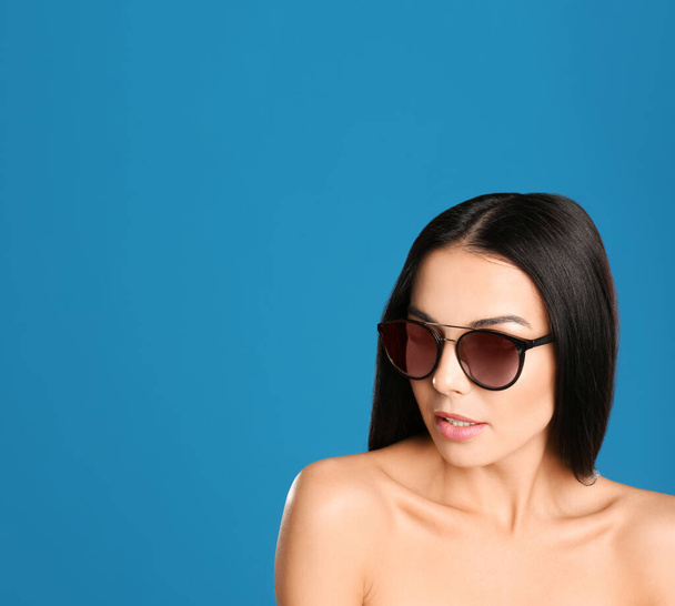 Beautiful woman wearing sunglasses on blue background. Space for text - Fotó, kép