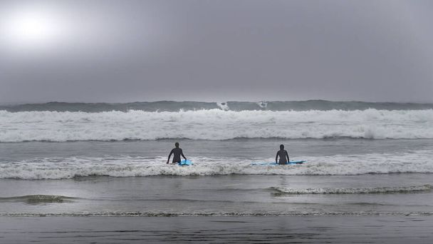 Surferzy zmierzający w kierunku fal w gęstej mgle, aby surfować w zatoce Cox w Parku Narodowym Pacific Rim na wyspie Vancouver, Kolumbia Brytyjska, Kanada - Zdjęcie, obraz