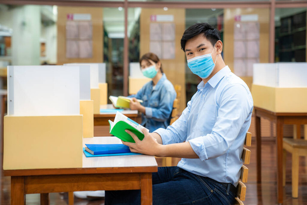 Two Asian university students wearing face mask and sitting and smile in library social distance from other 6 feets to avoid the spread of coronavirus in University. - Фото, зображення