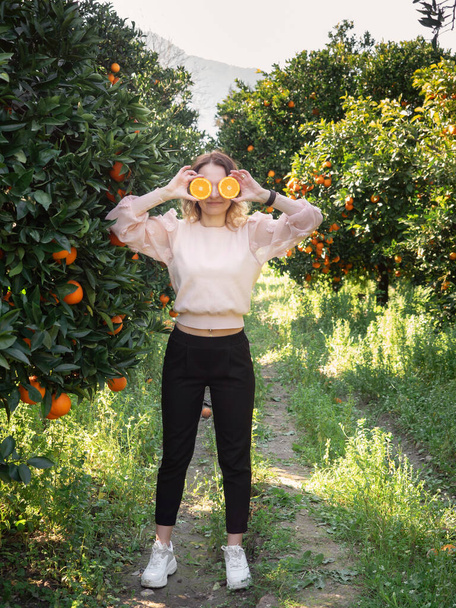 Young pretty woman holding oranges in front of eyes in the garden - Foto, Bild