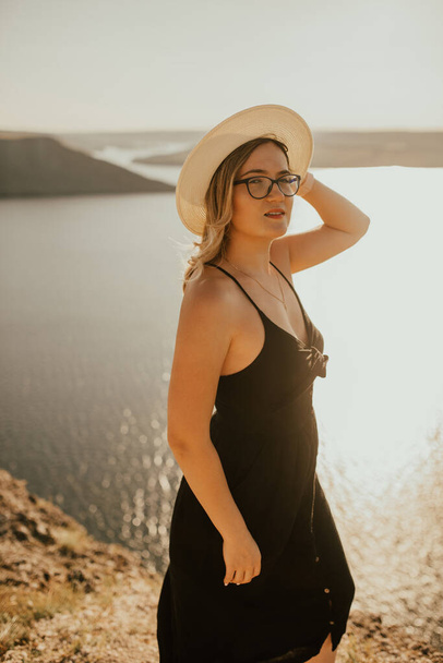 femme avec chapeau et lunettes se tient sur une falaise au-dessus de la mer - Photo, image