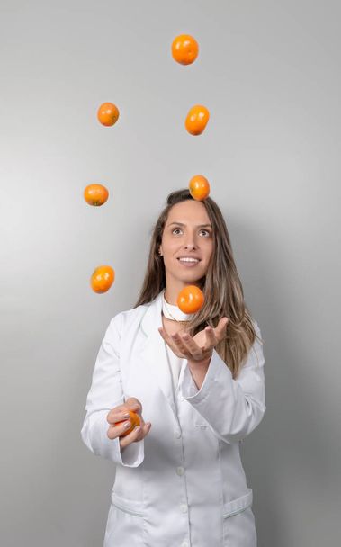 Lächelnde Ernährungsberaterin, die mit Orangen jongliert. Gesundheits- und Ernährungskonzept. Lebensstil. - Foto, Bild