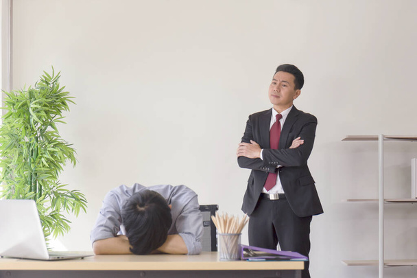 Азиатский руководитель-мужчина энергично стоял за своими подчиненными, которые спали на рабочем столе. - Фото, изображение