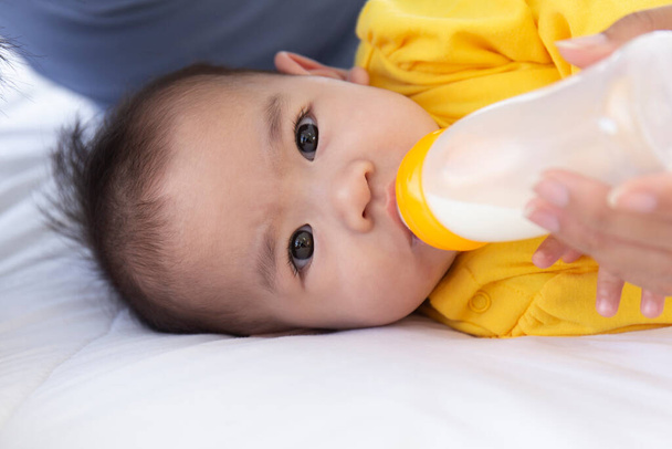 An Asian baby is bottle-fed in bed. - Foto, Bild