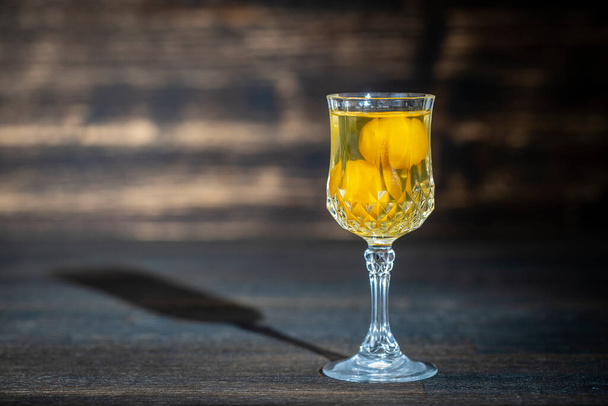 Tintura casera de ciruela de cereza amarilla en copa de cristal de vino sobre fondo de madera, Ucrania, espacio para copiar, de cerca. concepto de bebidas alcohólicas de bayas - Foto, Imagen