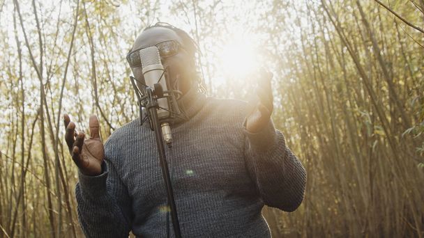 Young affrican man singing in the nature, sun rays coming through the trees - Foto, afbeelding