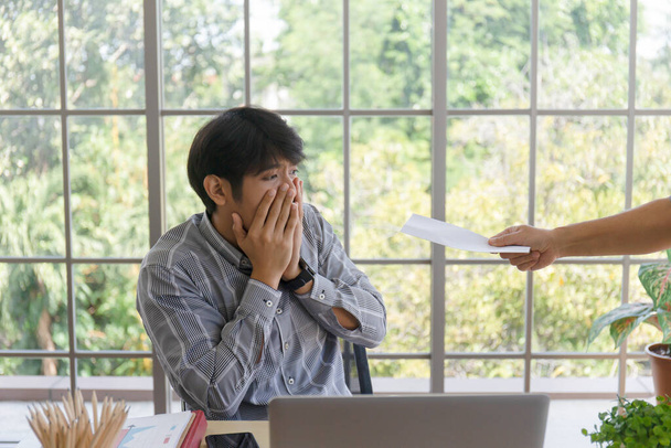A hand that delivers documents to a grieving Asian man with bad news: A desperate entrepreneur gets laid off, hides crying, disappointed by bankruptcy, business failure, or fired - Foto, Imagen